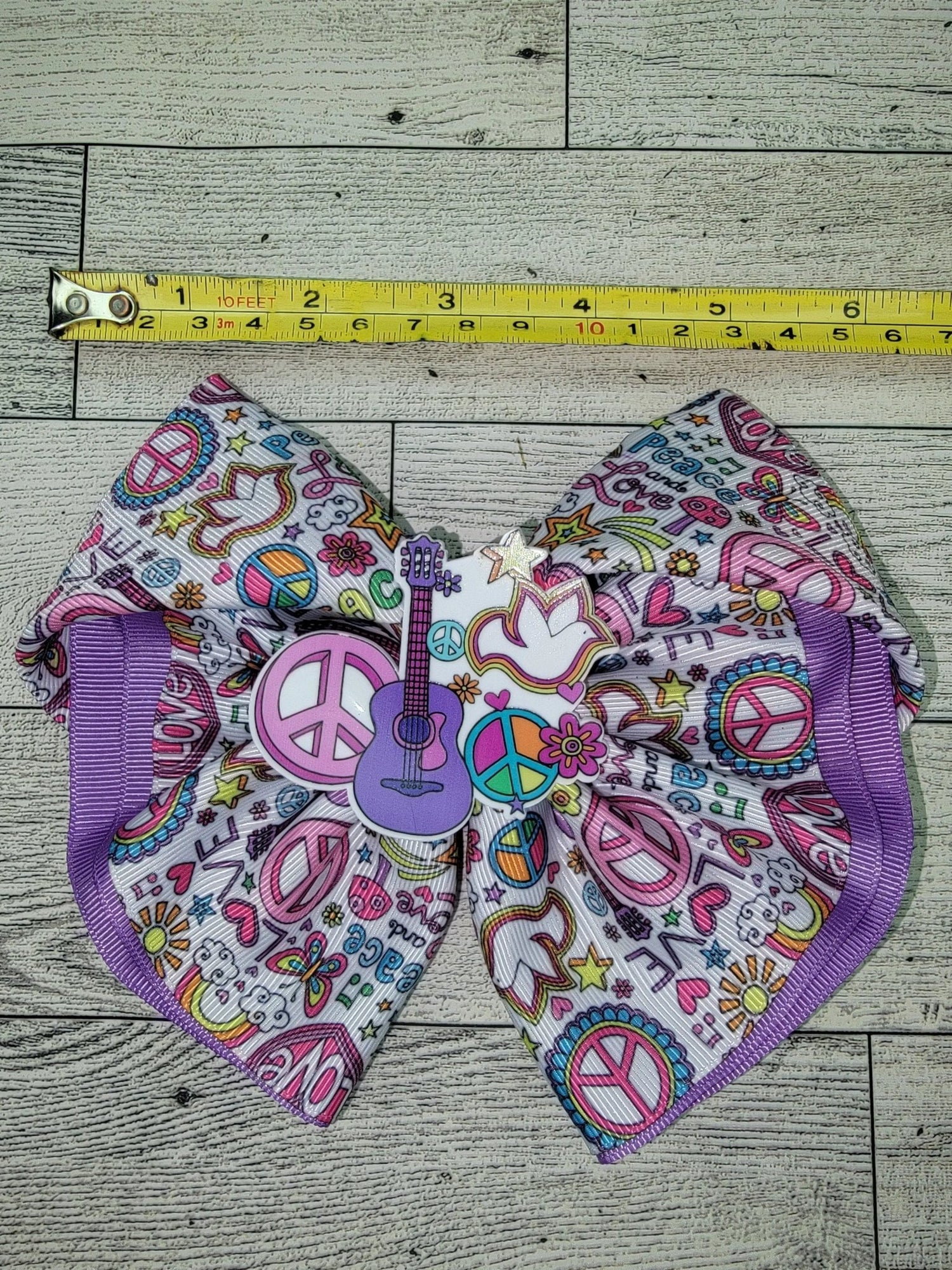 Colorful fabric with peace signs, hearts, and other patterns on a wooden surface with a measuring tape.