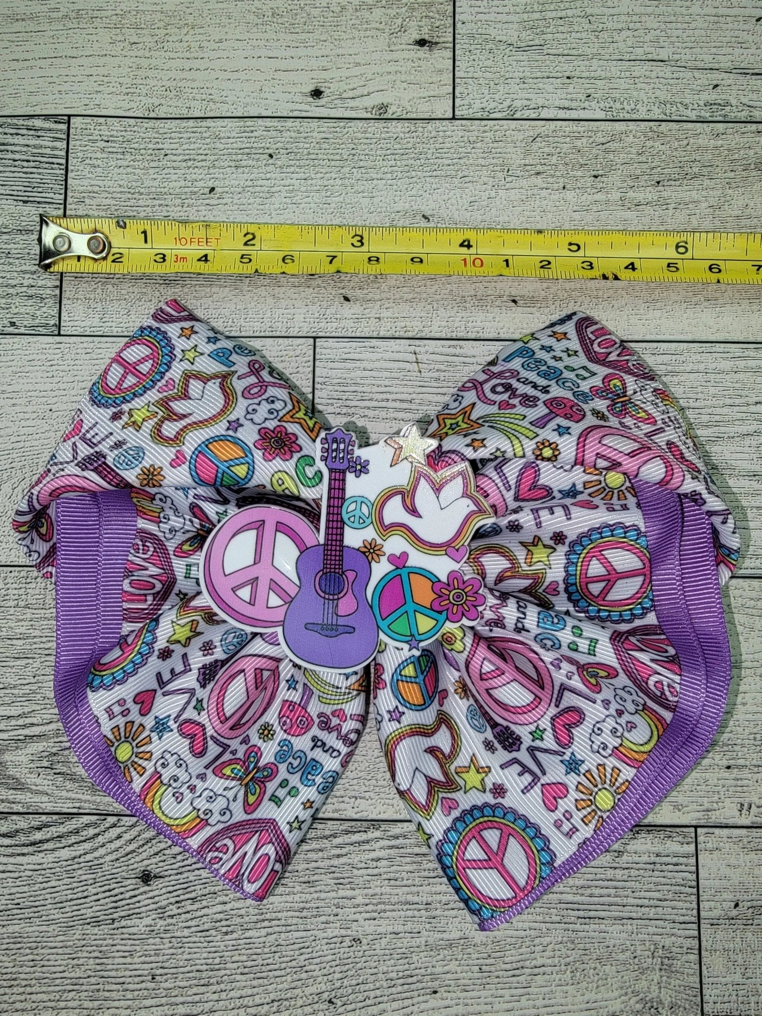 Colorful fabric with peace signs, hearts, and other patterns on a wooden surface with a measuring tape.
