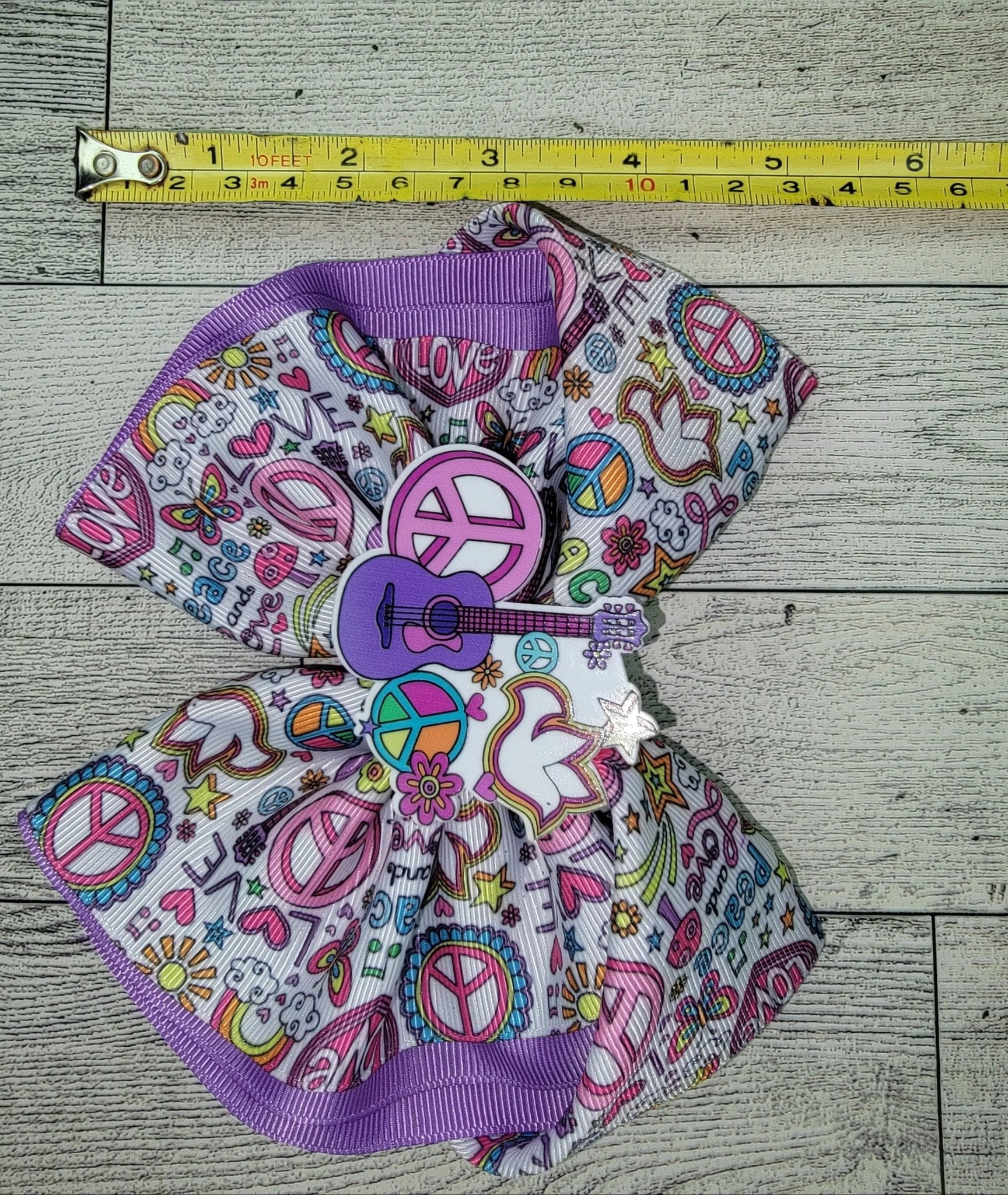 Colorful bow with peace signs and a guitar on a wooden surface with a measuring tape.