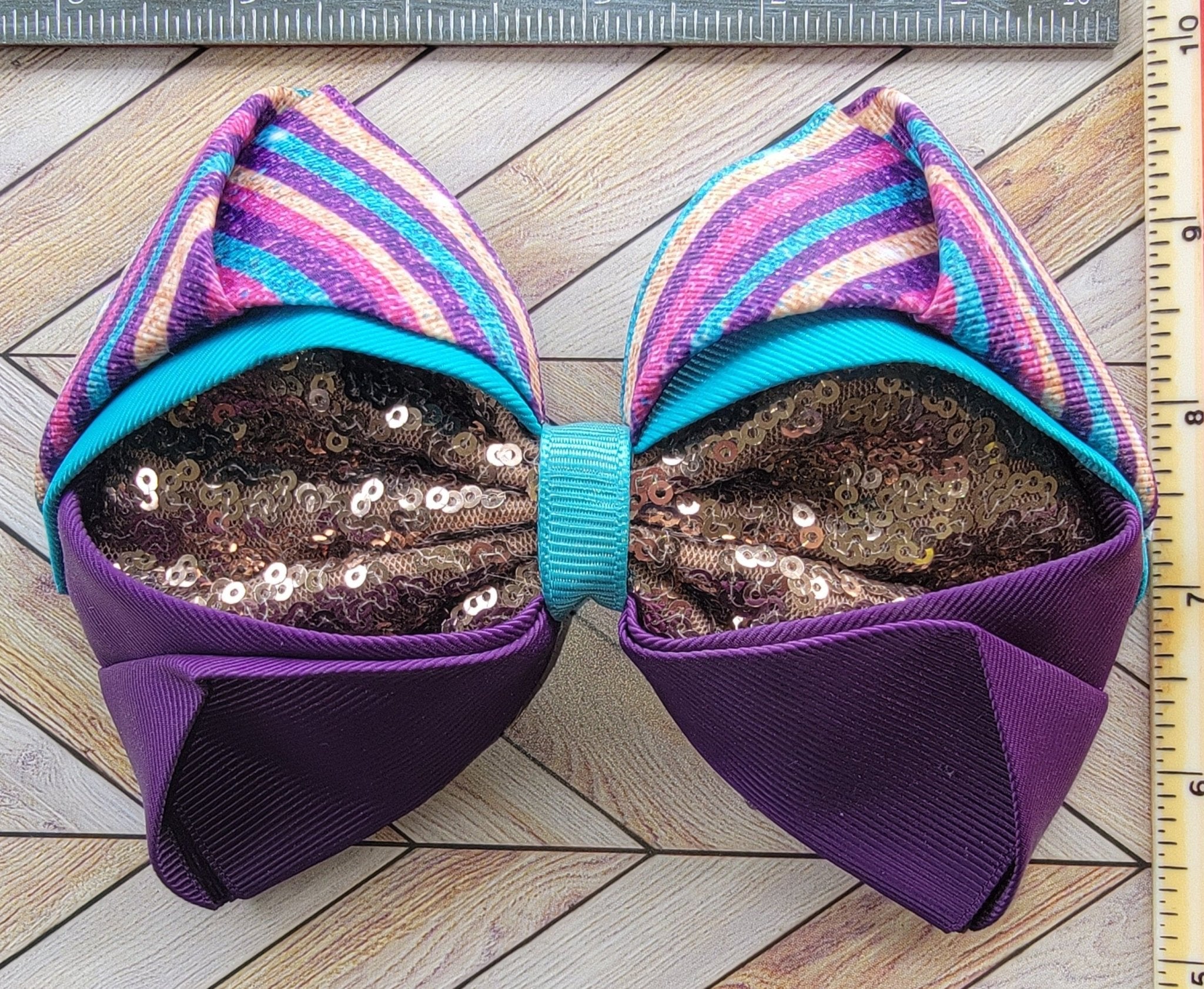 Large decorative bow with sequins on a wooden surface next to a ruler for scale.