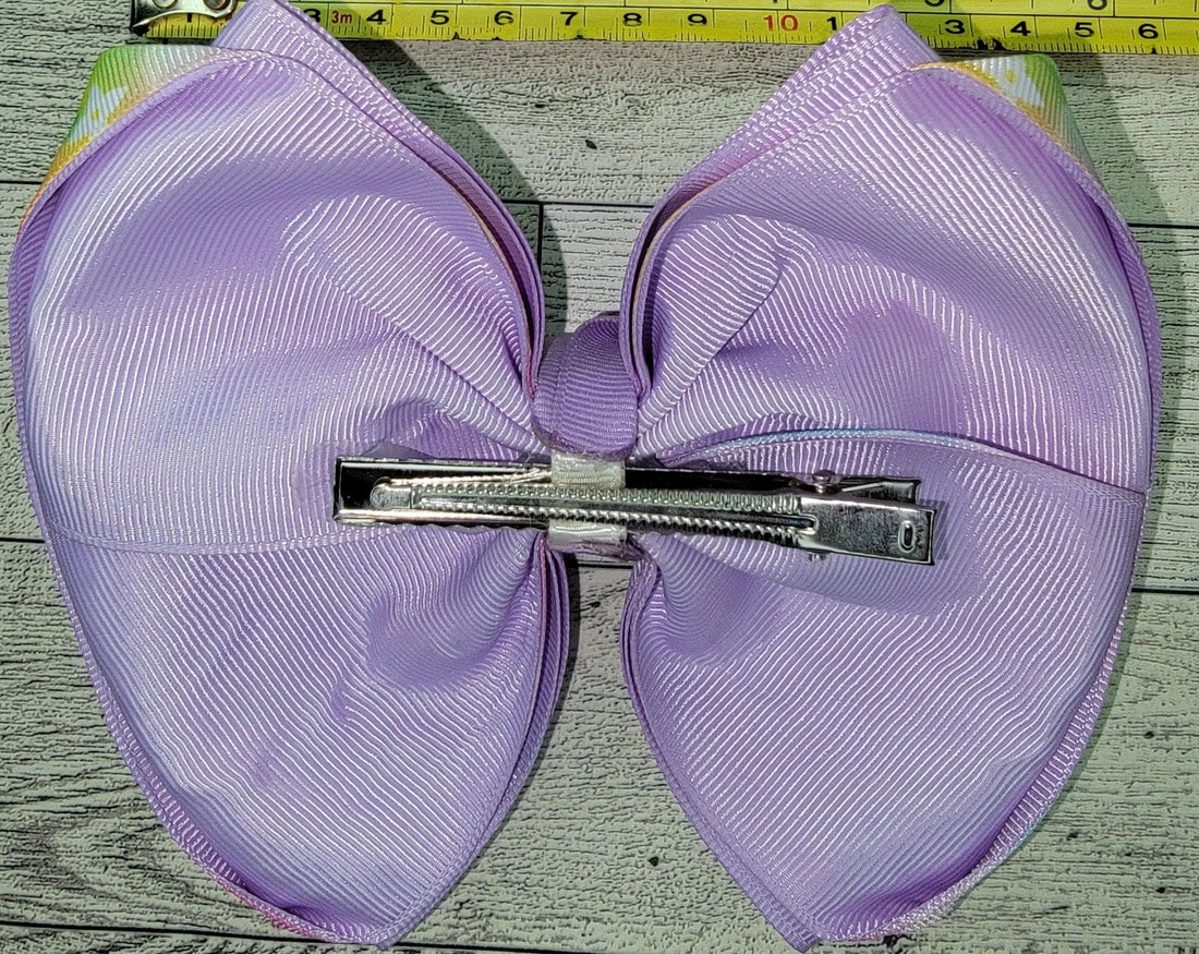 Purple hair bow with a clip on a wooden surface with a tape measure for scale.