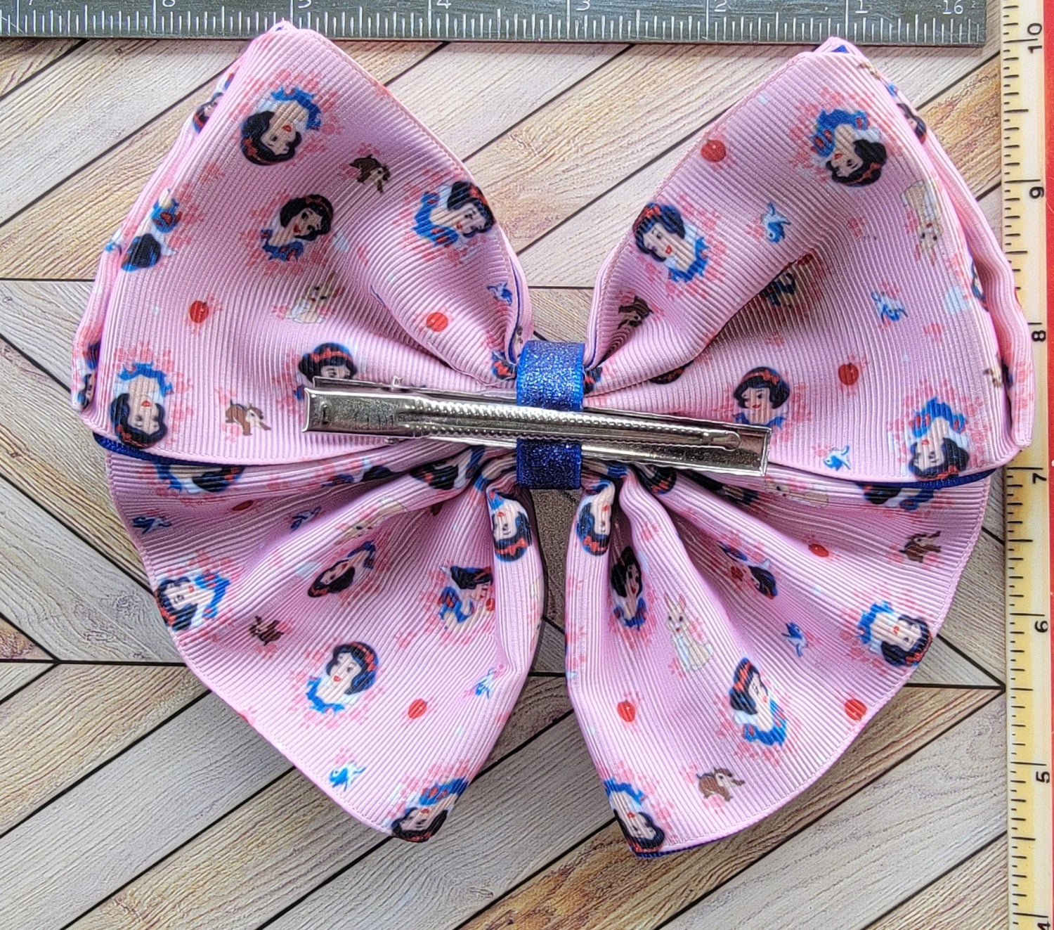 Pink bow with character print on a wooden surface with a ruler for scale.