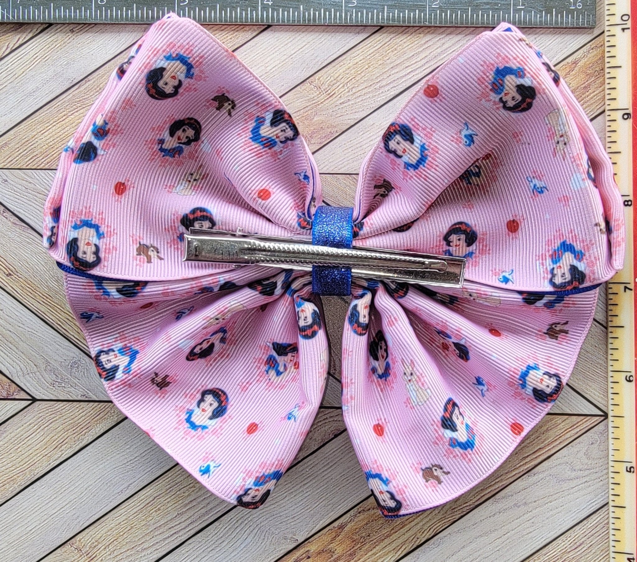 Pink bow with character print on a wooden surface with a ruler for scale.