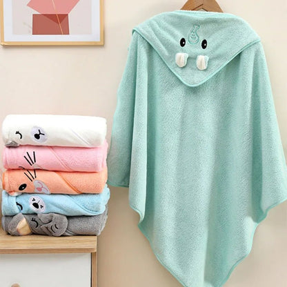Stack of colorful baby towels with a green hooded towel featuring cartoon face design on a beige surface.