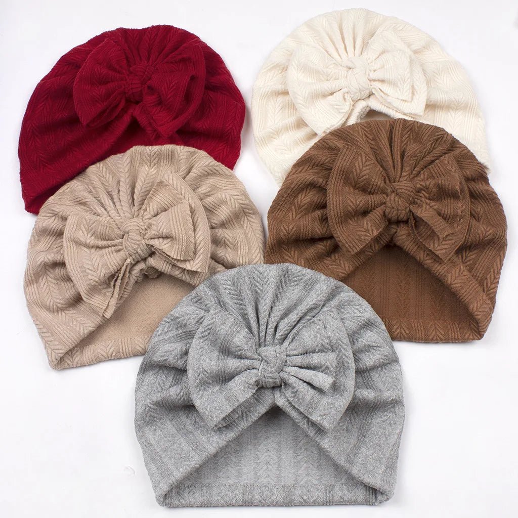 Five knit turbans in red, beige, white, brown, and gray on a white background