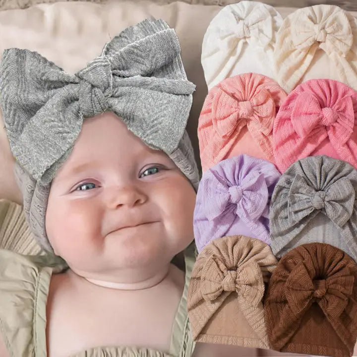 Baby wearing a gray headband with a bow, surrounded by various colored headbands.