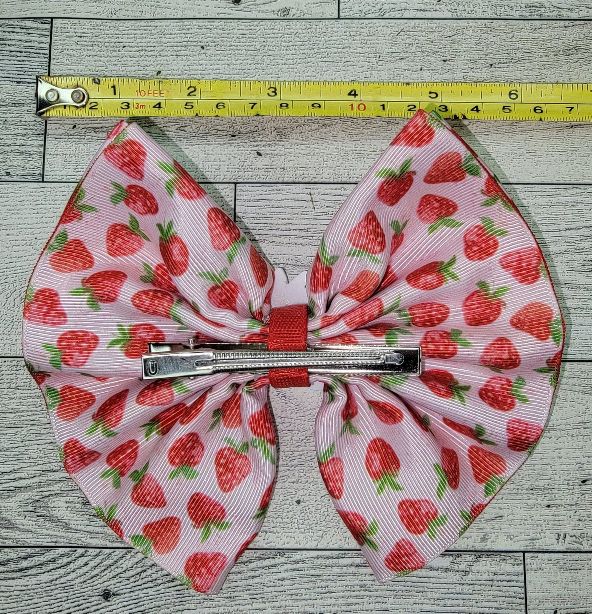Hair bow with strawberry pattern on a wooden surface with a tape measure for scale.