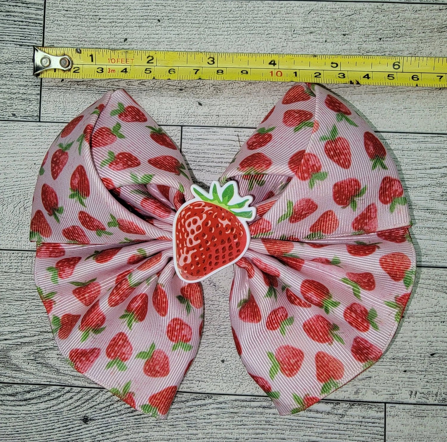 Hair bow with strawberry pattern on a wooden surface with a measuring tape.