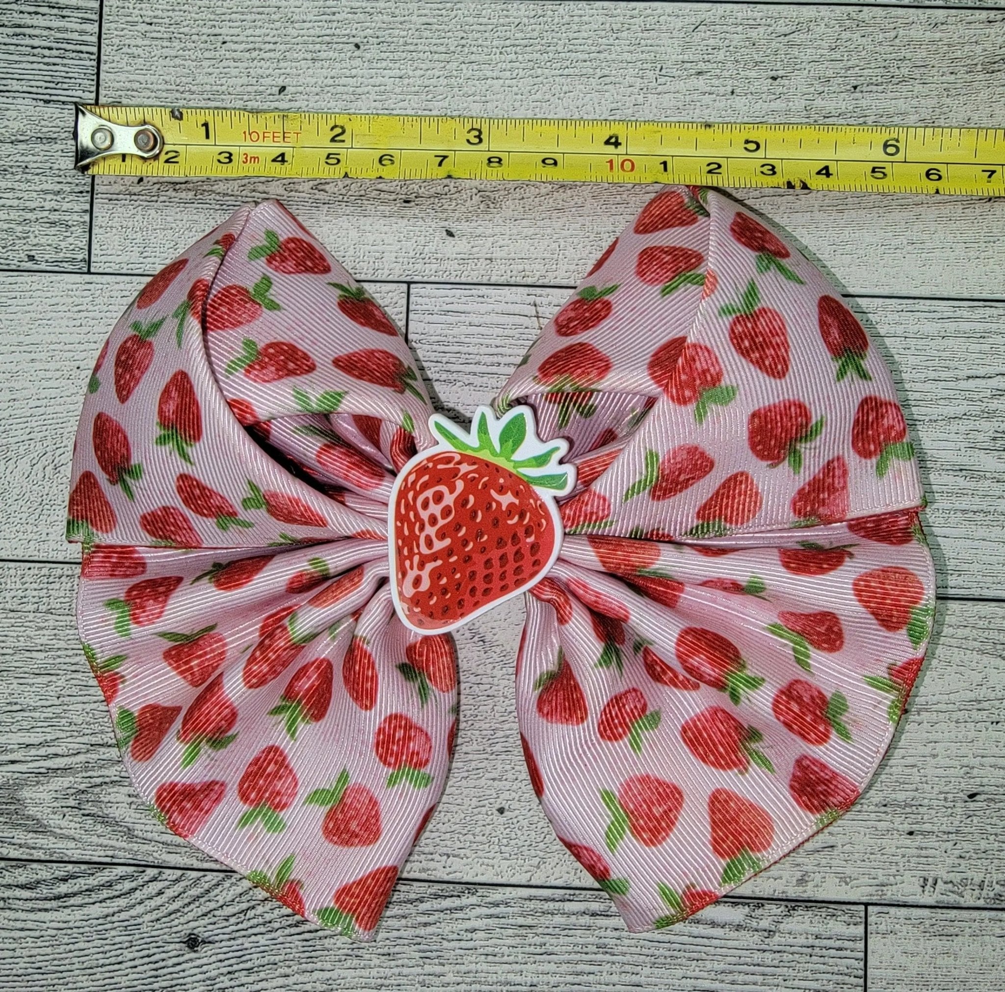 Hair bow with strawberry pattern on a wooden surface with a measuring tape.