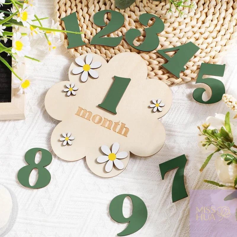 Wooden month calendar numbers arranged on a white textured fabric with daisy flowers and a woven placemat. The central flower-shaped plaque reads &
