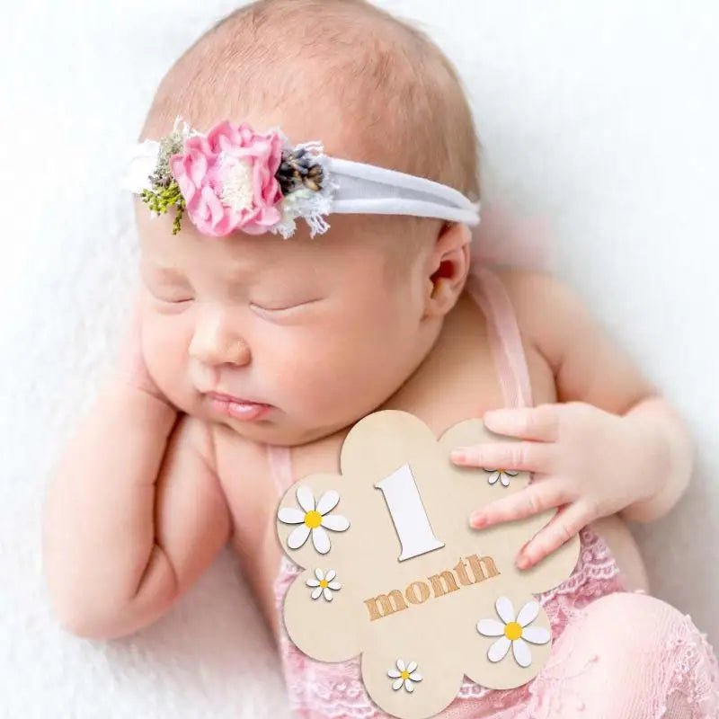 Newborn baby wearing a floral headband and holding a &