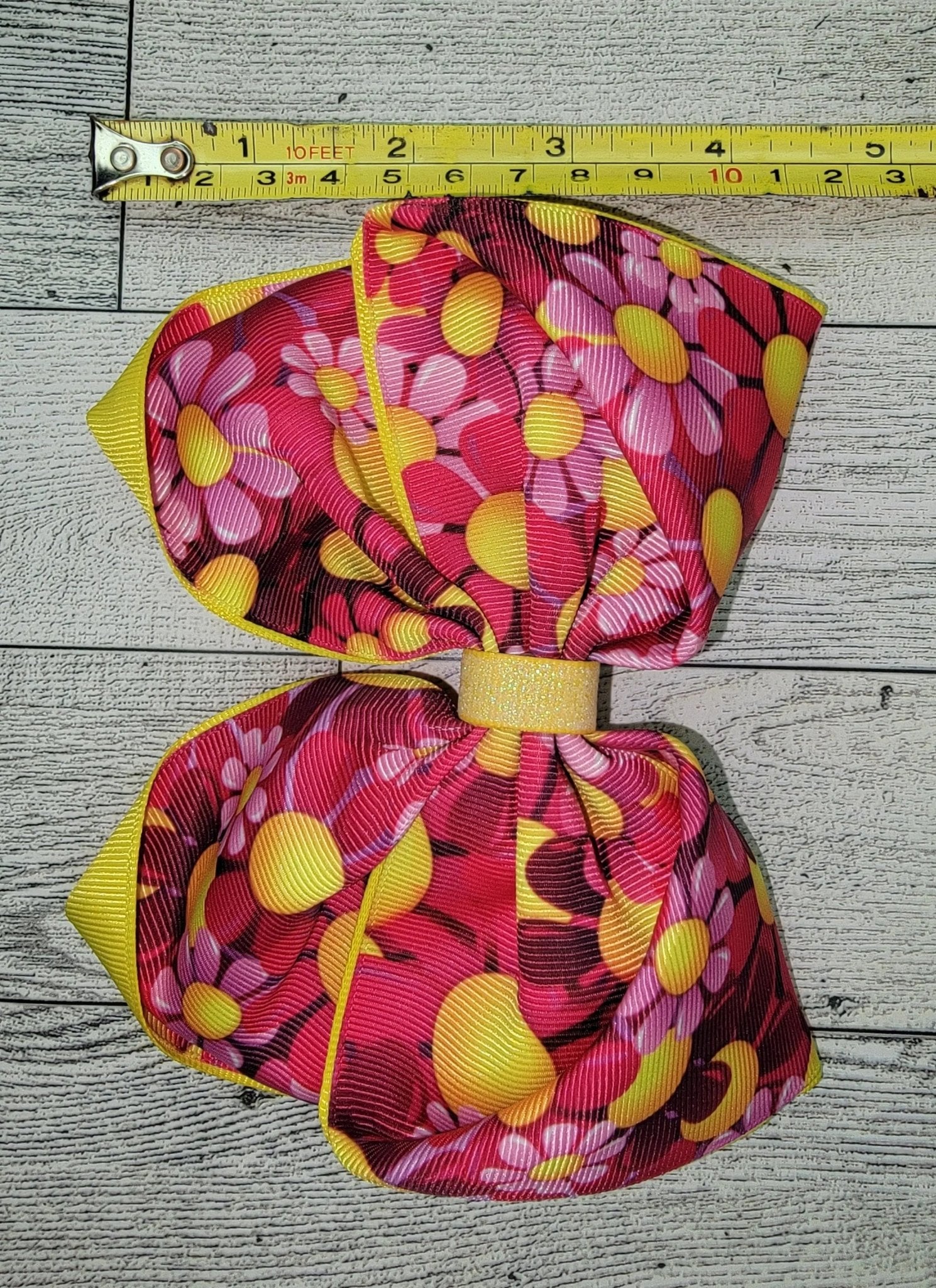 Colorful floral-patterned bow with a measuring tape for scale on a wooden surface