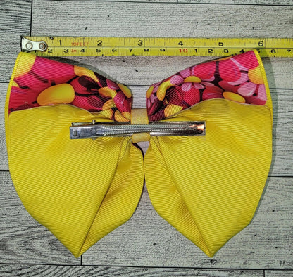Yellow hair bow with pink floral center and a hair clip on a wooden surface, measured by a tape measure.